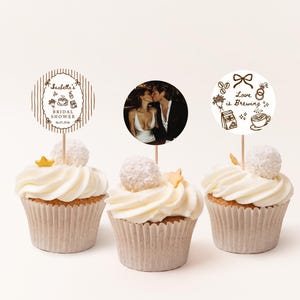Peut inclure: Trois cupcakes avec gla&ccedil;age blanc, chacun surmont&eacute; d'un &eacute;l&eacute;ment d&eacute;coratif. L'un pr&eacute;sente une photo d'un couple, un autre un topper "Bridal Shower", et le dernier dit "Love is Brewing".