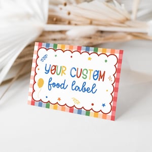Puede incluir: Una etiqueta de comida rectangular con un centro blanco festoneado y un borde de cuadros arco&iacute;ris. El texto "YOUR CUSTOM food label" aparece en letras multicolores, rodeado de peque&ntilde;os iconos gr&aacute;ficos de un globo, estrellas y confeti.