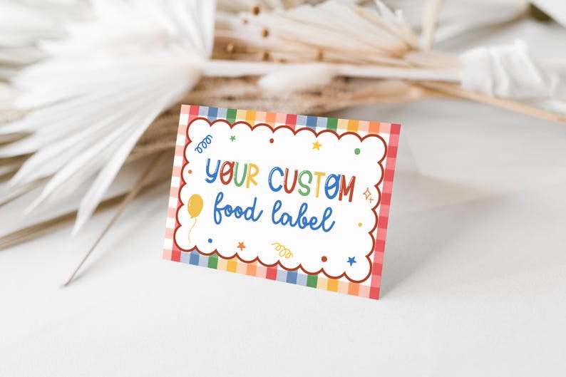 Puede incluir: Una etiqueta de comida rectangular con un centro blanco festoneado y un borde de cuadros arco&iacute;ris. El texto "YOUR CUSTOM food label" aparece en letras multicolores, rodeado de peque&ntilde;os iconos gr&aacute;ficos de un globo, estrellas y confeti.