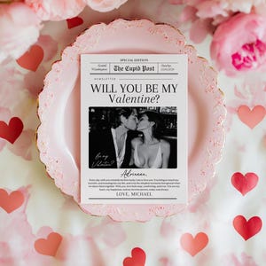May include: A Valentine's Day card with the headline "WILL YOU BE MY VALENTINE?" and a black and white photo of a couple kissing. The card is on a pink plate, surrounded by pink flowers and red heart cutouts.