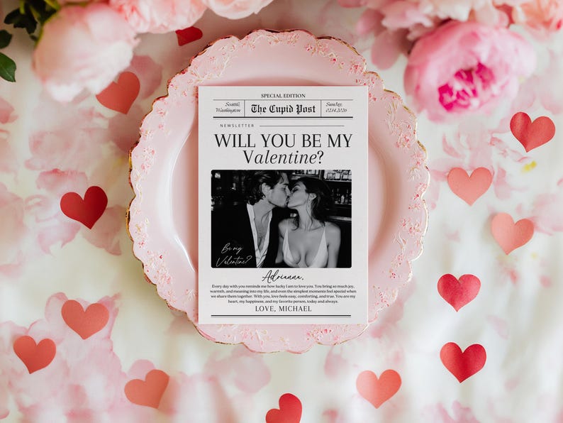 May include: A Valentine's Day card with the headline "WILL YOU BE MY VALENTINE?" and a black and white photo of a couple kissing. The card is on a pink plate, surrounded by pink flowers and red heart cutouts.