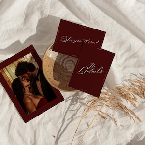 May include: A burgundy invitation suite with a photo of a couple kissing, and two cards with the phrases "See you there?" and "The Details" in elegant script. The items are arranged on a white, textured surface.