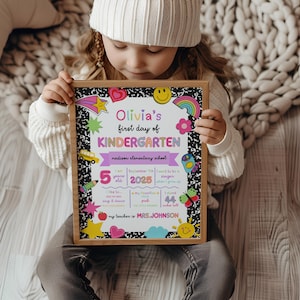 K&ouml;nnte beinhalten: Ein gerahmtes Schild mit dem Text "Olivia's first day of KINDERGARTEN" in Rosa und Gr&uuml;n. Das Schild enth&auml;lt einen Schulbus, einen Regenbogen und andere farbenfrohe Grafiken. Das Schild enth&auml;lt auch den Text "5 Jahre alt" und "112 cm gro&szlig;".