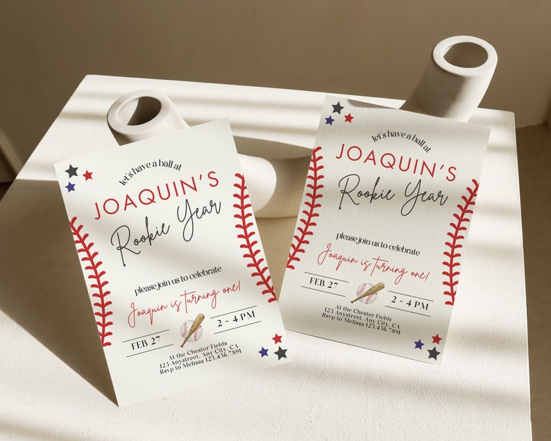 May include: Baseball-themed first birthday party invitation with red and white stitching, stars, and a baseball and bat graphic. The invitation reads "Let's have a ball at Joaquin's Rookie Year. Please join us to celebrate Joaquin is turning one!" with the date and time of the party.