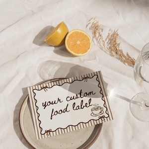 Peut inclure: Une tasse en c&eacute;ramique blanche avec une anse noire et l'inscription "But First, Coffee" en noir, dans une police manuscrite. La tasse est pos&eacute;e sur une surface blanche.