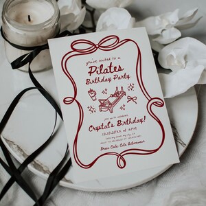 May include: A Pilates birthday party invitation with a red border and text. The invitation includes the text "Pilates Birthday Party" and "Crystal's Birthday!" A candle in a glass jar and white flowers are in the background.