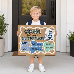 May include: A rectangular sign made of brown paper with a white scalloped border, featuring the text Carter's first day of Kindergarten, I am 5 years old, Date August 2026, I want to be a Firefighter, and I like to play sports and play videogames.