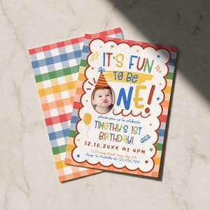 Puede incluir: Una tarjeta de invitaci&oacute;n de cumplea&ntilde;os rectangular con un borde blanco festoneado, una foto de un ni&ntilde;o con gorro de fiesta y texto colorido que dice IT'S FUN TO BE ONE! TIMOTHY'S 1ST BIRTHDAY! 12.10.20XX at 4PM. El reverso tiene un patr&oacute;n de cuadros.