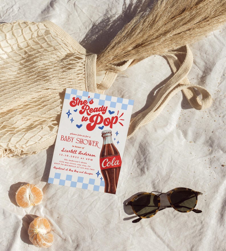 Puede incluir: Una invitaci&oacute;n a un baby shower con el texto "She's Ready to Pop" y una ilustraci&oacute;n de una botella de cola. La invitaci&oacute;n est&aacute; sobre un fondo a cuadros azul y blanco. Tambi&eacute;n se muestran gafas de sol, una bolsa de red, hierba seca y rodajas de naranja.