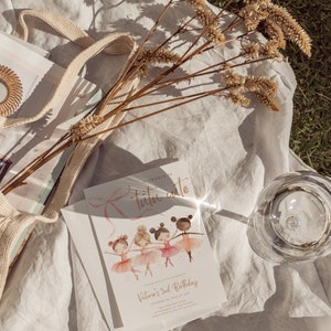 May include: A white invitation card with a pink ribbon and the text "Victoria's 2nd Birthday" in gold lettering. The card features an illustration of four ballerinas in pink tutus and sparkly shoes.