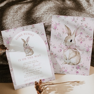 Op de afbeelding: Een roze en witte babyshower-uitnodiging met een bloemenpatroon en een aquarel-illustratie van een konijn. De uitnodiging luidt "Some Bunny is on the Way" en bevat de datum, tijd en locatie van de babyshower.