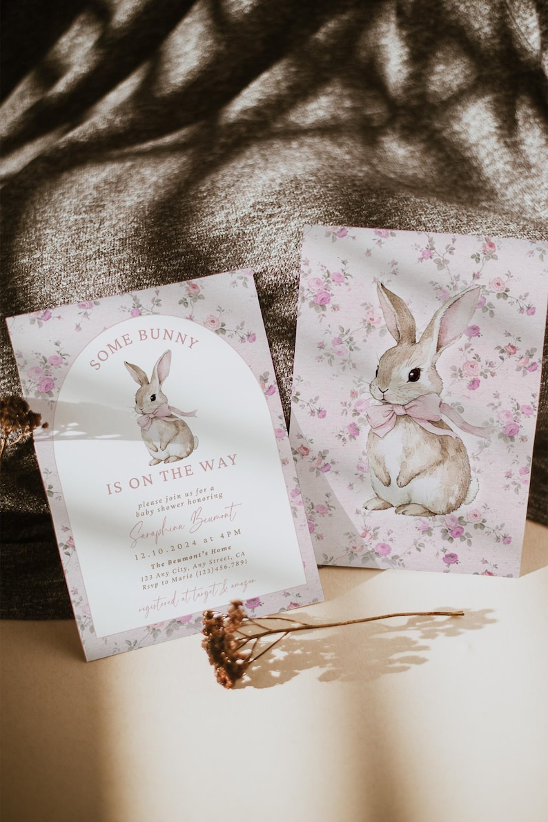 Op de afbeelding: Een roze en witte babyshower-uitnodiging met een bloemenpatroon en een aquarel-illustratie van een konijn. De uitnodiging luidt "Some Bunny is on the Way" en bevat de datum, tijd en locatie van de babyshower.