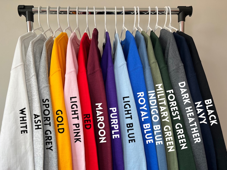 May include: A rack of 15 sweatshirts in various colors, including white, ash, sport grey, gold, light pink, red, maroon, purple, light blue, royal blue, indigo blue, military green, forest green, dark heather, navy, and black.