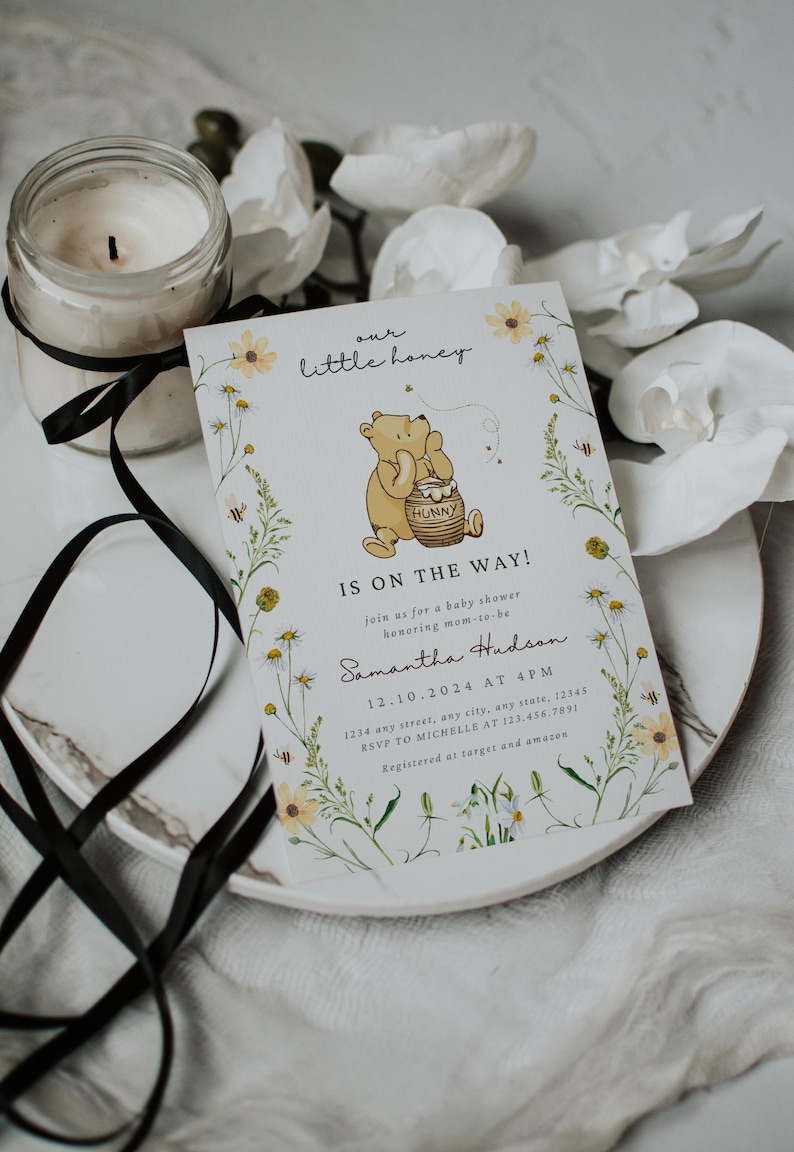 May include: A baby shower invitation with a Winnie the Pooh theme. The invitation features a cartoon bear holding a honey pot, surrounded by floral illustrations. The text reads "our little honey" and "IS ON THE WAY!"
