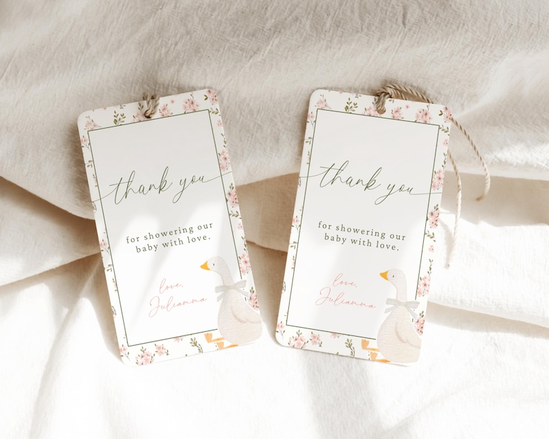 May include: Two white thank you tags with pink floral designs and a cartoon goose illustration. The text on the tags reads "thank you for showering our baby with love." and "Love, Julianna".