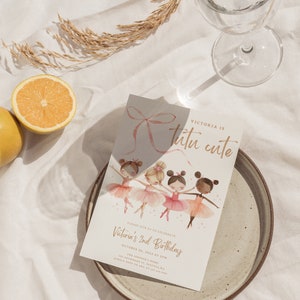 May include: A pink and gold birthday invitation with a watercolor illustration of four girls wearing tutus and holding pink ribbons. The text reads "Victoria is tutu cute" and "Please join us to celebrate Victoria's 2nd Birthday, October 04, 2024 at 3PM".