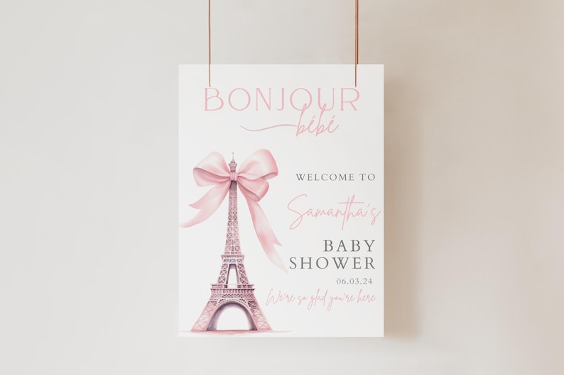 May include: A pink and white baby shower sign with a pink bow on top of the Eiffel Tower. The sign says "Bonjour Bibi" and "Welcome to Samantha's Baby Shower 06.03.24 We're so glad you're here."