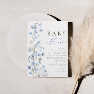 Puede incluir: Una invitaci&oacute;n a una fiesta de bienvenida al beb&eacute; con un dise&ntilde;o floral azul y el texto "Baby in Bloom". La invitaci&oacute;n incluye el nombre Victoria Rivera, la fecha 18 de junio de 2023, la hora 1:00 PM, la ubicaci&oacute;n Daisy Ballroom, la direcci&oacute;n 1234 Tulip Road, San Diego, CA 92114, y la informaci&oacute;n de RSVP.