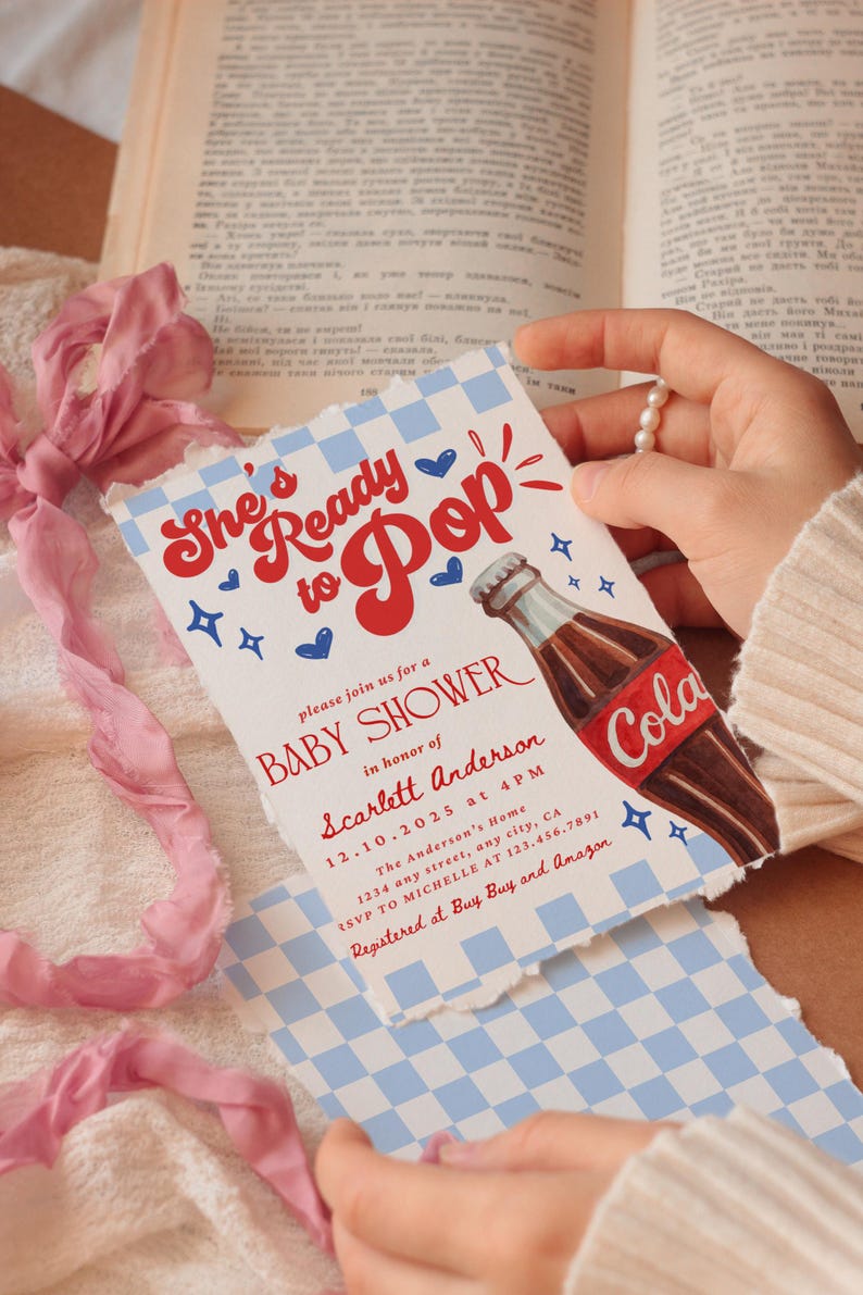 Puede incluir: Invitaci&oacute;n a un baby shower con un dise&ntilde;o retro. La invitaci&oacute;n presenta el texto "She's Ready to Pop" en rojo, junto con una ilustraci&oacute;n de una botella de cola. El fondo tiene un patr&oacute;n de cuadros azules y blancos.