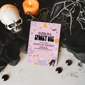 Puede incluir: Invitaci&oacute;n a una fiesta de Halloween rosa y naranja con el texto "Olivia is a Spooky One" y "Olivia's 1st Birthday". La invitaci&oacute;n presenta un sombrero de bruja, un caldero, un gato negro y otras ilustraciones de tem&aacute;tica de Halloween.