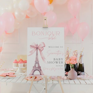 Puede incluir: Un cartel de baby shower rosa y blanco con el texto "Bonjour b&eacute;b&eacute;" y una ilustraci&oacute;n de acuarela de la Torre Eiffel con un lazo rosa. El cartel tambi&eacute;n incluye el texto "Bienvenido a la baby shower de Samantha 06.03.24 Estamos encantados de que est&eacute;s aqu&iacute;."
