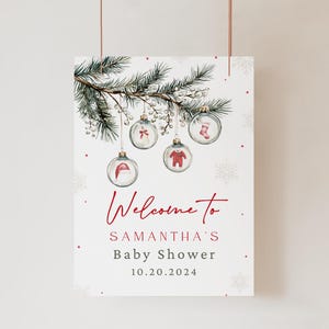 K&ouml;nnte beinhalten: Ein wei&szlig;es Willkommensschild mit rotem Text, auf dem steht "Willkommen zu Samanthas Baby Shower 10.20.2024". Das Schild zeigt eine Aquarell-Illustration eines Kiefernzweigs mit Ornamenten. Die Ornamente sind aus klarem Glas mit roten und wei&szlig;en Illustrationen einer Baby-M&uuml;tze, eines Baby-Bodys, einer Baby-Socke und einer Schleife.