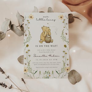May include: Baby shower invitation featuring Winnie the Pooh with a honey pot. The invitation reads "Our Little Honey, Is on the Way!" and includes event details. Floral and bee illustrations frame the text on a cream background.