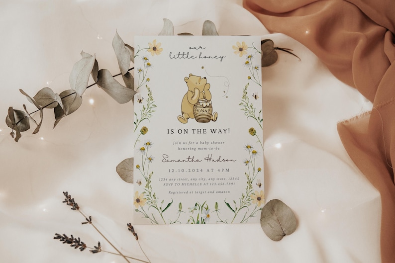 May include: Baby shower invitation featuring Winnie the Pooh with a honey pot. The invitation reads "Our Little Honey, Is on the Way!" and includes event details. Floral and bee illustrations frame the text on a cream background.