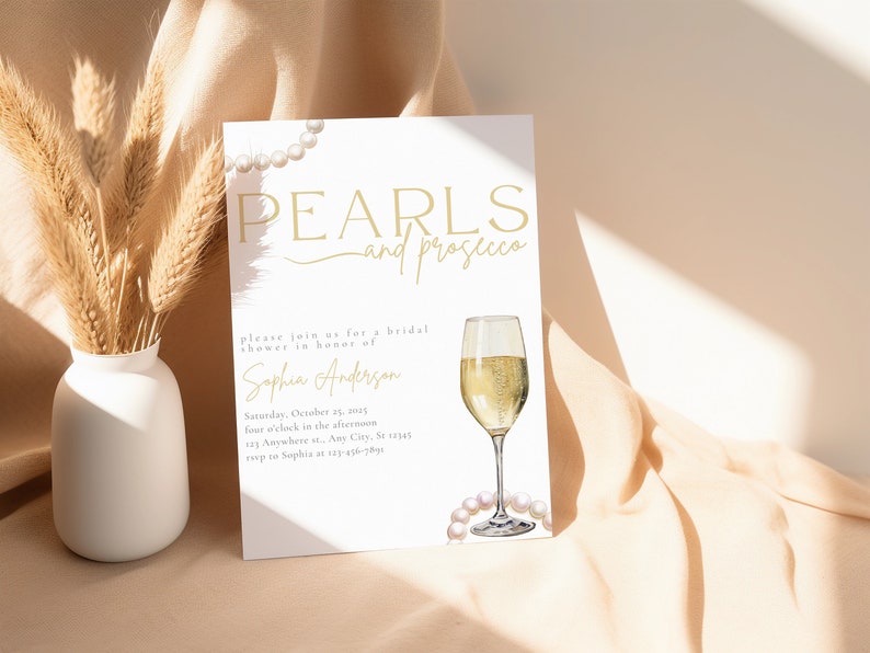 May include: A white invitation card with gold text that reads "Pearls and Prosecco" and a watercolor illustration of a glass of champagne and pearls. The invitation is for a bridal shower in honor of Sophia Anderson. The date and time of the shower are listed as Saturday, October 25, 2023 at four o'clock in the afternoon. The address is listed as 123 Anywhere St., Any City, St 12345. The RSVP information is listed as "roup to Sophia at 123&epsilon;&tau;ά&sigma;&theta;&alpha;&iota;".