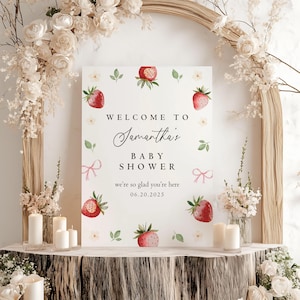 May include: Welcome to Samantha's Baby Shower sign with a watercolor strawberry design. The sign is white with black text and pink bows. The date of the shower is 06.20.2025.