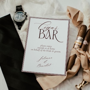May include: A white rectangular sign with a dark red border and text that reads Cigar BAR, please enjoy outside or at home on behalf of the bride & groom, Julianna & Benedict, accompanied by a black necktie, a black wristwatch, and two cigars.