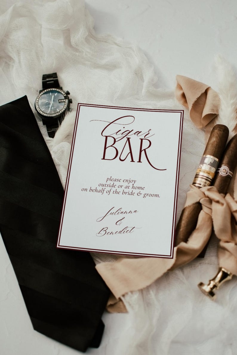 May include: A white rectangular sign with a dark red border and text that reads Cigar BAR, please enjoy outside or at home on behalf of the bride & groom, Julianna & Benedict, accompanied by a black necktie, a black wristwatch, and two cigars.