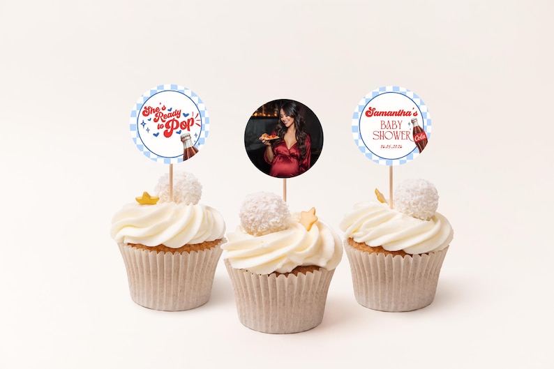 Może przedstawiać: Trzy babeczki z białym lukrem, każda zwieńczona ozdobnym patyczkiem. Dwa patyczki mają tekst: "She's Ready to Pop" i "Samantha BABY SHOWER 25.06.2026". Środkowa babeczka ma zdjęcie osoby.