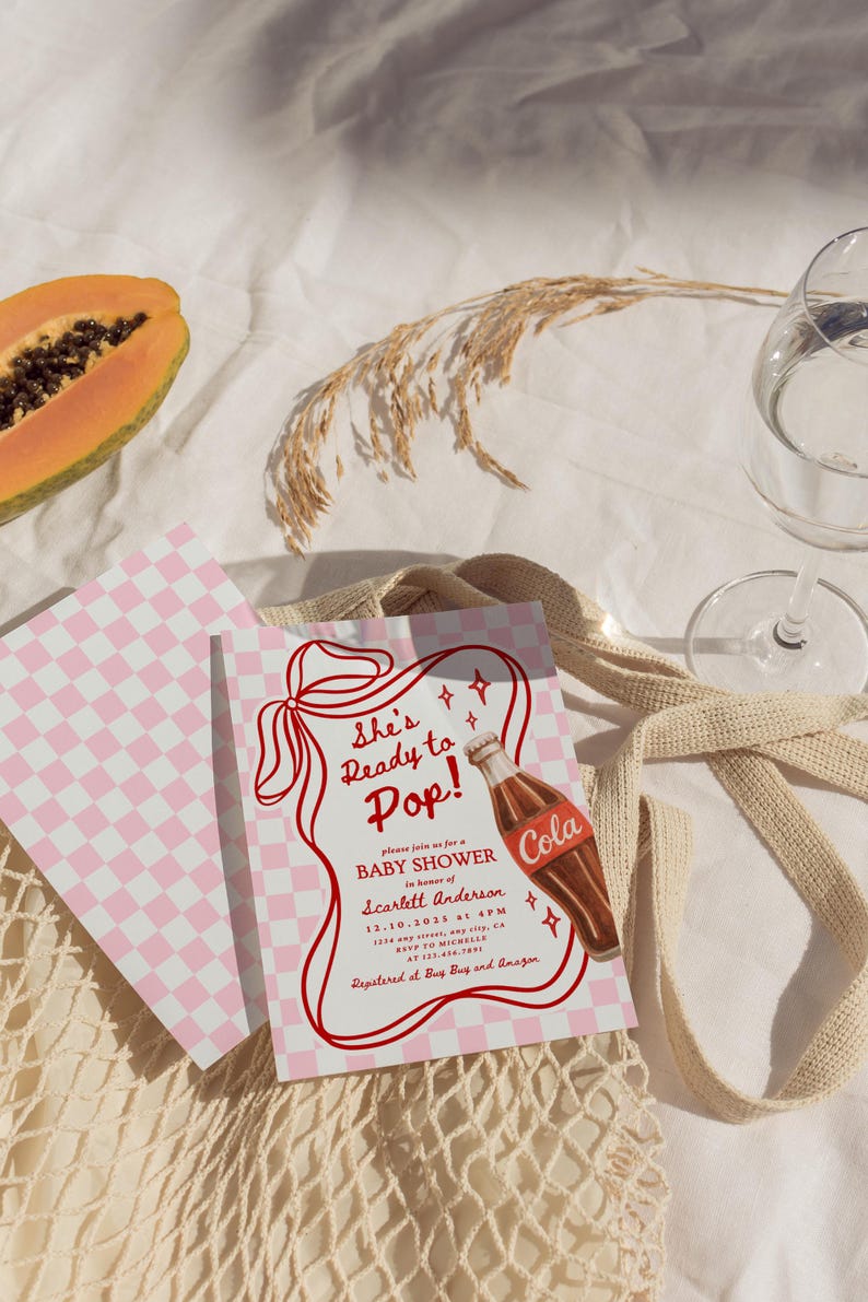 Puede incluir: Invitaci&oacute;n a un baby shower con un patr&oacute;n de cuadros rosas y blancos y el texto "She's Ready to Pop!". Se presenta un gr&aacute;fico de botella de cola vintage. La invitaci&oacute;n est&aacute; sobre una superficie blanca con una papaya y un vaso de agua.