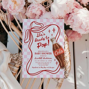 Puede incluir: Invitaci&oacute;n a un baby shower con un fondo a cuadros rosa y blanco. La invitaci&oacute;n presenta el texto "She's Ready to Pop!" y una ilustraci&oacute;n de una botella de cola. La invitaci&oacute;n est&aacute; rodeada de flores rosas.