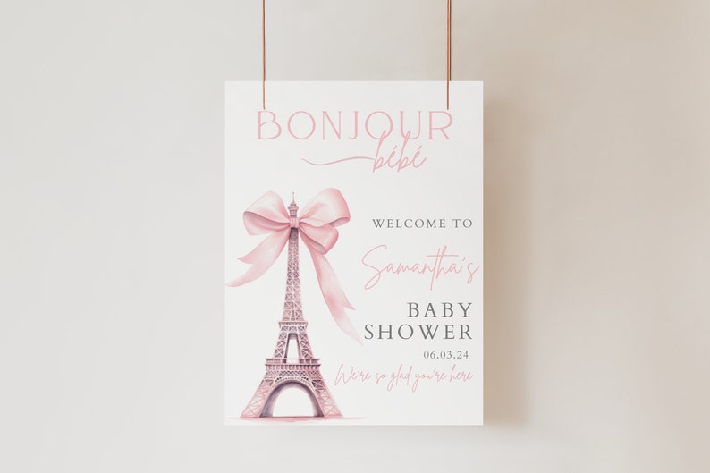 Puede incluir: Un cartel de bienvenida rosa y blanco con el texto "Bonjour Bibi" y un lazo rosa en la parte superior de la Torre Eiffel. El texto "Bienvenido a la Baby Shower de Samantha 06.03.24 Estamos encantados de que est&eacute;s aqu&iacute;" tambi&eacute;n est&aacute; en el cartel.