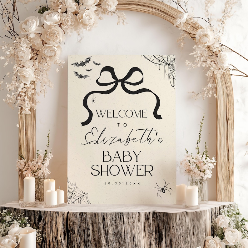 K&ouml;nnte beinhalten: Cremefarbenes Babyparty-Schild mit schwarzen Akzenten. Auf dem Schild steht "Willkommen zu Elizabeths Babyparty" mit dekorativen Flederm&auml;usen, Spinnen und Spinnweben. Das Schild ist mit Blumen und Kerzen dekoriert.