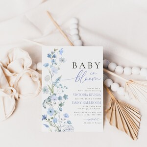Puede incluir: Una invitaci&oacute;n a un baby shower con un dise&ntilde;o floral de acuarela en tonos azules y morados. El texto dice "Baby in Bloom" e incluye el nombre Victoria Rivera, la fecha 03 de junio de 2023, la hora 4:00 PM, la ubicaci&oacute;n Daisy Ballroom, la direcci&oacute;n 1234 Tulip Road, San Diego, CA 2014, y la informaci&oacute;n de RSVP.