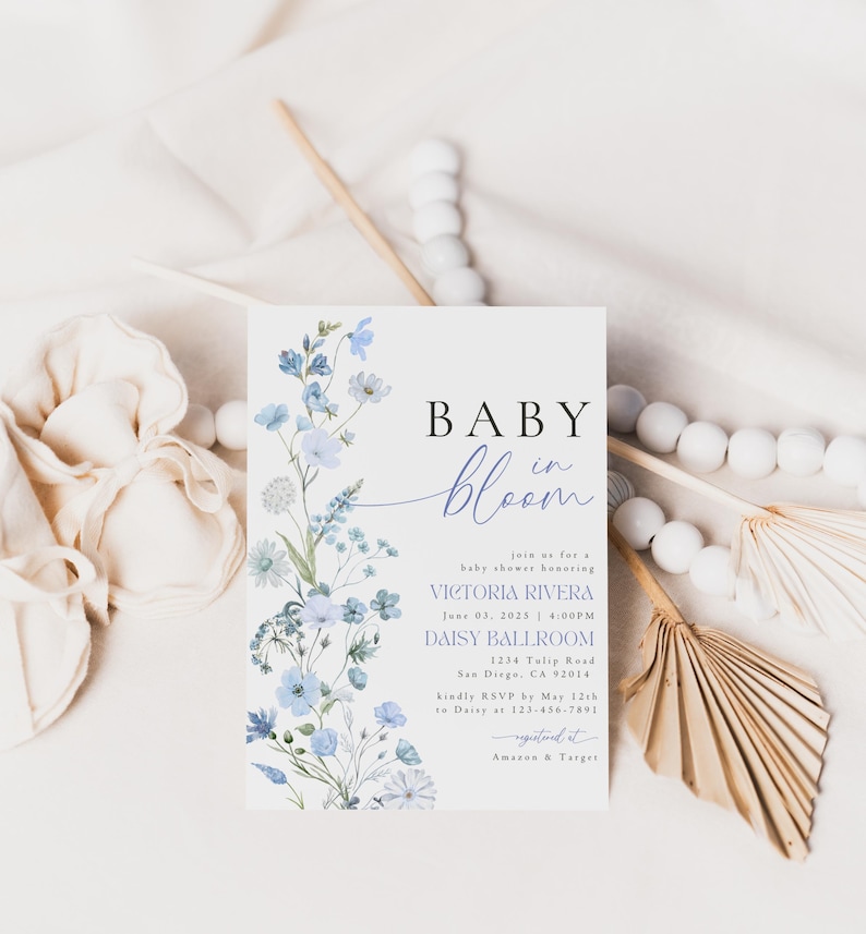 Puede incluir: Una invitaci&oacute;n a un baby shower con un dise&ntilde;o floral de acuarela en tonos azules y morados. El texto dice "Baby in Bloom" e incluye el nombre Victoria Rivera, la fecha 03 de junio de 2023, la hora 4:00 PM, la ubicaci&oacute;n Daisy Ballroom, la direcci&oacute;n 1234 Tulip Road, San Diego, CA 2014, y la informaci&oacute;n de RSVP.