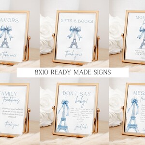 May include: Set of ten 8x10 inch printable signs for a Parisian themed baby shower. The signs feature a watercolour illustration of the Eiffel Tower with a blue ribbon. The signs include text such as "Favors", "Gifts & Books", "Mom-osa Bar", "Family Traditions", "Don't Say Baby", and "Message from the Bump".