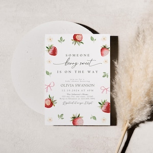 May include: A white baby shower invitation with a strawberry theme. The invitation features a watercolor illustration of strawberries and flowers. The text reads "Someone berry sweet is on the way." The invitation also includes the date, time, and location of the shower.