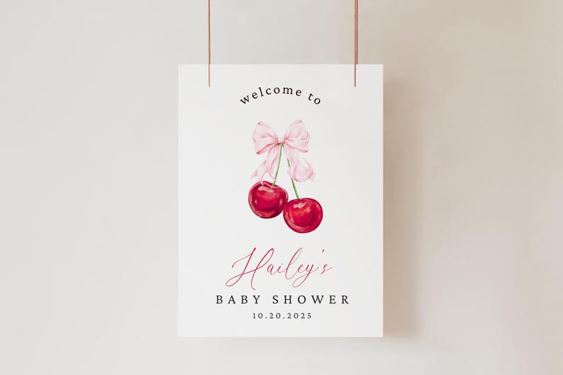May include: A white sign with the text "welcome to Hailey's Baby Shower 10.20.2025" in black and pink. A pink bow with two red cherries are illustrated above the text.
