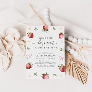May include: A baby shower invitation with a watercolor illustration of strawberries and white flowers. The text reads "Someone berry sweet is on the way" and includes the name Olivia Swanson, the date and time of the shower, and the location.