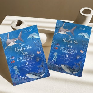 May include: Two invitation cards with an "Under the Sea" theme. The cards feature illustrations of sharks, dolphins, and other marine life against a blue background. The text reads "Join Us Under the Sea, Sebastian is turning 4!" and includes the date October 14.