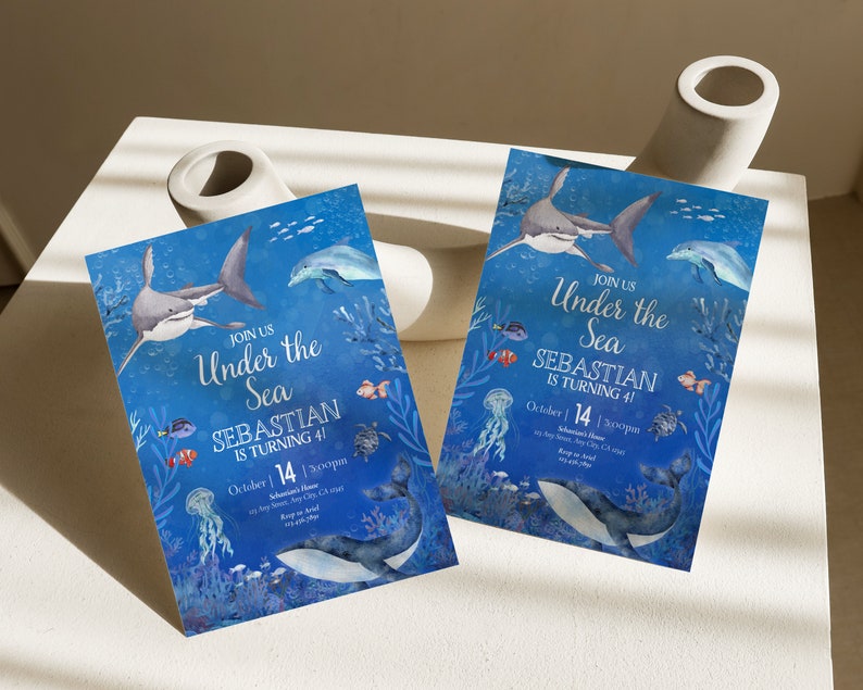 May include: Two invitation cards with an "Under the Sea" theme. The cards feature illustrations of sharks, dolphins, and other marine life against a blue background. The text reads "Join Us Under the Sea, Sebastian is turning 4!" and includes the date October 14.