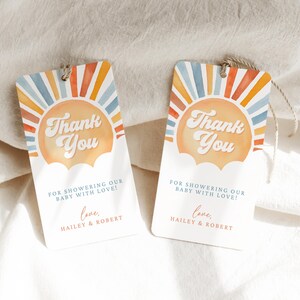 May include: Two thank you tags with a watercolor sunset design. The text on the tags reads "Thank You" with a retro font. The text below the sun says "For showering our baby with love! Love, Hailey & Robert."