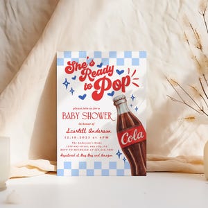 Puede incluir: Una invitaci&oacute;n para un baby shower con un tema retro. La invitaci&oacute;n presenta el texto "She's Ready to Pop" en rojo y azul, junto con una ilustraci&oacute;n de una botella de cola. La invitaci&oacute;n incluye detalles para el baby shower de Scarlett Anderson.