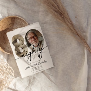 May include: An 80th birthday invitation with a photo of a baby and an older man. The invitation is on textured paper with the word "eighty" in cursive. The invitation includes event details.