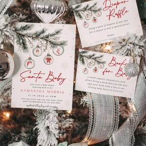 K&ouml;nnte beinhalten: Eine Weihnachts-Babyparty-Einladung mit einem roten und wei&szlig;en Farbschema. Die Einladung zeigt eine Aquarell-Illustration eines Kiefernzweigs mit Ornamenten. Der Text lautet "Santa Baby" und enth&auml;lt den Namen der werdenden Mutter, das Datum und die Uhrzeit der Party sowie die Adresse. Die Einladung enth&auml;lt auch Informationen &uuml;ber die Geschenkregistrierung und die RSVP.