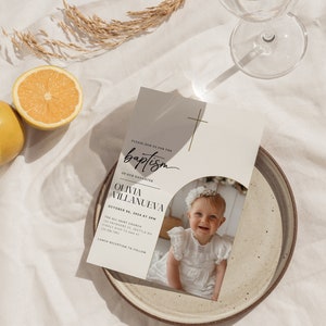 May include: A white baptism invitation with a gold cross and a photo of a baby girl in a white dress. The invitation reads "Please join us for the baptism of our daughter Olivia Villanueva October 06, 2024 at 3PM The All Saint Church 123 Anywhere St. Seattle WA Kindly RSVP to Ana at 123-456-7891 Lunch reception to follow"